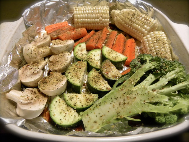Multiple veggies sprayed, dusted, on foil in casserole dish before roasting