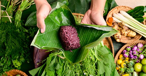 Hands wrapping purple sticky rice in banana leaves